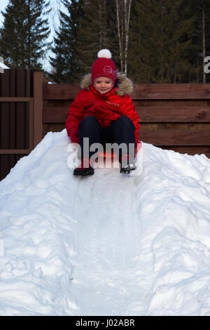 Girl glisse vers le bas de la colline de neige sur une soucoupe Banque D'Images