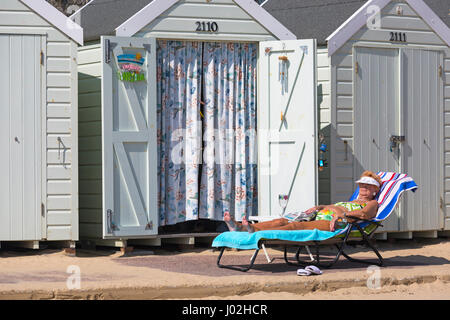 Bournemouth, Dorset, UK. Apr 9, 2017. Météo France : belle chaude journée ensoleillée comme visiteurs chef de la mer à profiter du soleil sur les plages de Bournemouth. Femme mature de vous détendre sur une chaise longue à l'extérieur de cabane de plage avec du papier journal et de verre vide. Credit : Carolyn Jenkins/Alamy Live News Banque D'Images