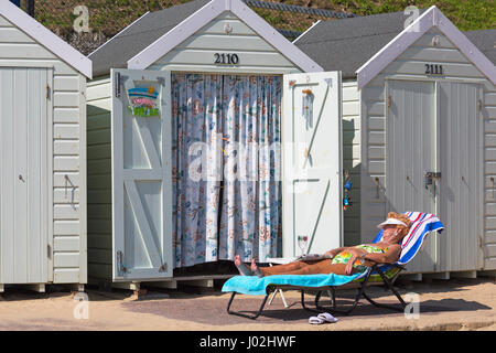 Bournemouth, Dorset, UK. Apr 9, 2017. Météo France : belle chaude journée ensoleillée comme visiteurs chef de la mer à profiter du soleil sur les plages de Bournemouth. Femme mature de vous détendre sur une chaise longue à l'extérieur de cabane de plage avec du papier journal et de verre vide. Credit : Carolyn Jenkins/Alamy Live News Banque D'Images