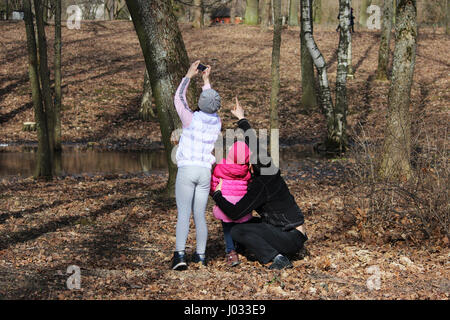 Pour une promenade en famille. Papa montre fille sur l'écureuil, qui siège sur arbre. Girl prend des photos de l'écureuil sur le téléphone. Banque D'Images