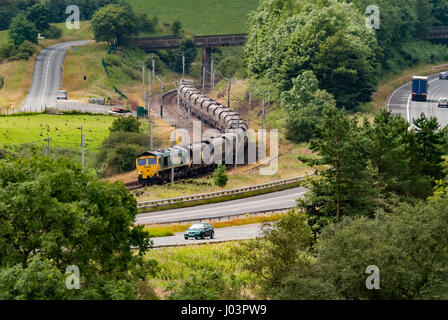 Locomotive de classe 66 transportant des wagons de freightliner sur la ligne principale de la côte ouest à Cumbria, en passant par l'autoroute M 6. Banque D'Images