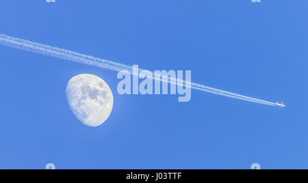 Lune gibbeuse à phase, avec un avion qui semble passer au-dessus, montrant les traînées de condensation et de ciel bleu. Banque D'Images