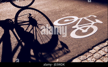 Ombre de méconnaissable le vélo cycliste sur piste cyclable à travers la ville à côté de la signalisation en milieu urbain entourant Banque D'Images