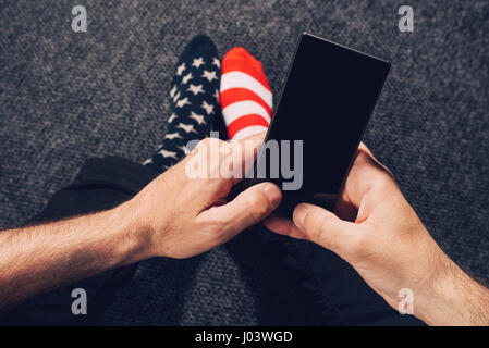 Des profils caucasian man wearing socks drapeau USA à l'aide de téléphone mobile tout en restant assis sur le sol Banque D'Images