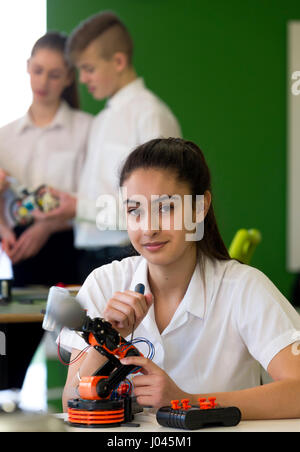 Adolescente, le design et la technologie dans une leçon. Elle sourit à l'appareil photo avec un bras robotique qu'elle est en face de son immeuble. Banque D'Images