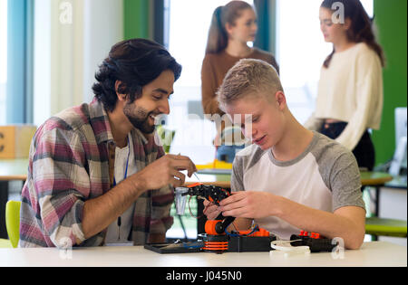 Étudiant et Enseignant travaillant sur un bras robotique dans une salle de classe. Il y a des étudiants debout dans l'arrière-plan. Banque D'Images