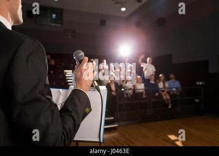 Enseignant de sexe masculin de faire un discours dans une salle de conférences. Il est debout à la tribune et certains élèves ont leur part jusqu'à poser une question. Banque D'Images