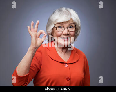 Smiling senior dame montrant ok signe sur fond gris Banque D'Images