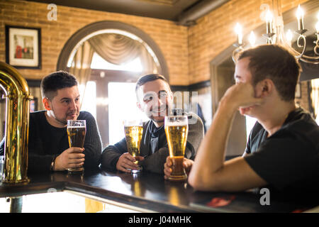 Cheerful vieux amis s'amuser et de boire la bière au comptoir du bar dans un pub. Banque D'Images