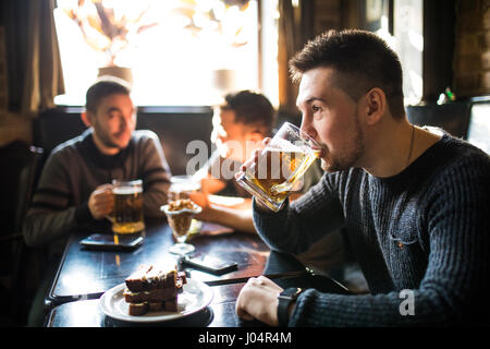 L'homme de boire de la bière devant à discuter entre amis boire dans un pub. Banque D'Images