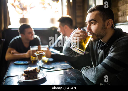 L'homme de boire de la bière devant à discuter entre amis boire dans un pub. Banque D'Images