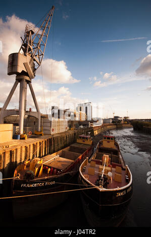 London, England - April 11, 2010: Two barges docked at a wharf on a small river. A crane and cargo ocupy the wharf. Shot on Deptford Creek beside the  Banque D'Images