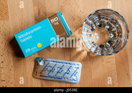 Un paquet de Nitrofurantoin tablets utilisé pour le traitement des infections de la vessie sur une table de chevet avec un verre d'eau. Un antibiotique. Banque D'Images