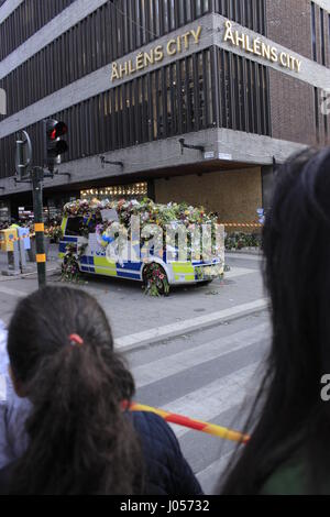 Les piétons à la recherche dans le cadre de la populaire place emplacement dans Ahlens mall, avec le Suédois Polis, voiture de police dans l'arrière-plan, couvert de fleurs de condoléances à pileup les Suédois nation aux victimes du 7 avril 2017, attaque le terrorisme de Stockholm, Stockholm, Suède. Banque D'Images