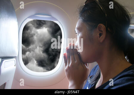 Priant les passagers dans un avion volant tout en regardant par la fenêtre sur les nuages de tempête. Banque D'Images