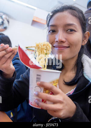 Jeune femme de manger des aliments à partir d'une tasse de papier dans la salle à manger dans le magasin.Asian girl eating lunch avec noodle à table dans la restauration rapide. Banque D'Images