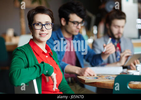 Portrait of young businesswoman wearing glasses réussie et looking at camera, smiling, travaillant avec des collègues Banque D'Images