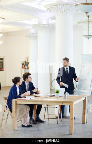 Les collègues de travail assis par table et parler à businessman presenting graphiques de tableau blanc Banque D'Images