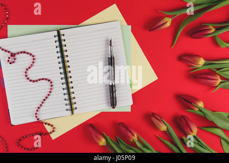 Ouvrir bloc-notes papier et stylo avec rouge printemps tulipes fleurs sur fond rouge Banque D'Images
