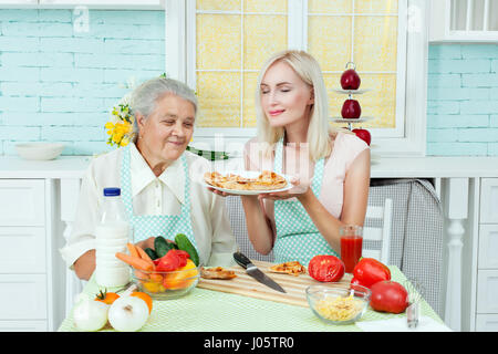 Grand-mère et femme renifla de pizza fraîchement cuites, elles sont femmes au foyer. Banque D'Images