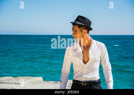 Bel homme en chemise blanche et chapeau sur la plage Banque D'Images