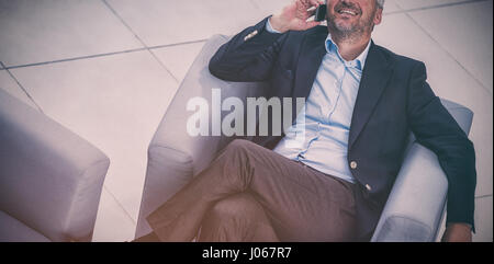 Businessman assis sur une chaise et talking on mobile phone in office Banque D'Images