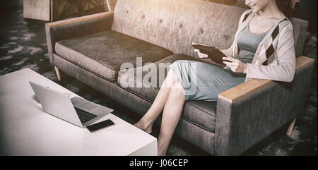 Femme business executive sitting on sofa using digital tablet Banque D'Images