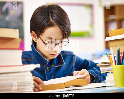 L'école primaire asiatique garçon portant des lunettes la lecture d'un livre épais. Banque D'Images