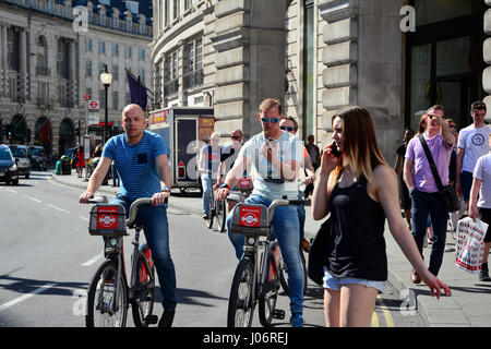 Young Woman talking on smartphone marche à travers Road en face d'hommes sur Borris bikes Banque D'Images