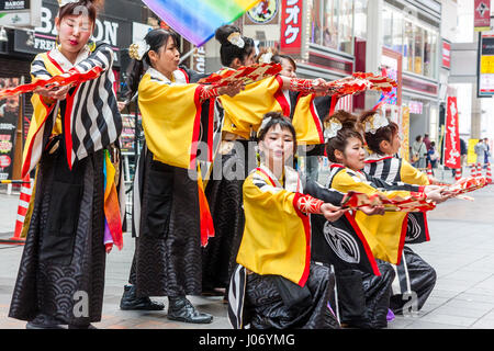 Le Japon, Kumamoto, Hinokuni danse Yosakoi Festival. L'équipe de femmes adolescentes, vêtu de noir et jaune, s'agenouiller et yukata holding fans, dans centre commercial. Banque D'Images