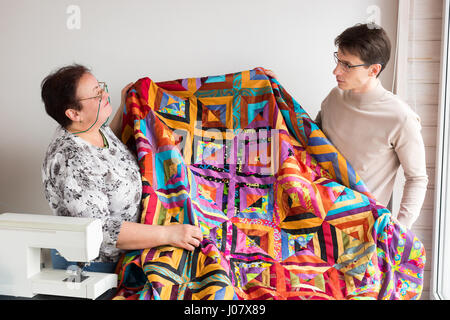 Atelier de courtepointe de tailleurs - homme et femme tailleurs ensemble tenant dans leur mains un grand tissage produit, fabriqué à partir de morceaux de tissu de couleur sur Banque D'Images