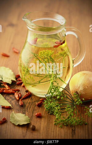 Carafe avec de l'huile et des épices comme la feuille de piment et l'oignon sur table en bois. Banque D'Images