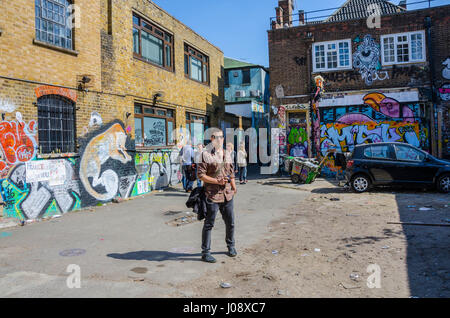 Un touriste se distingue et admire l'art de la rue sur les murs d'un parking gratuit juste à côté de Brick Lane dans l'Est de Londres. Banque D'Images