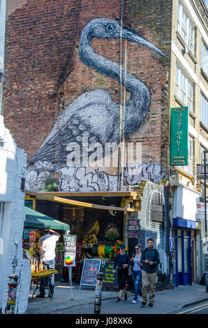 La cuisine végétalienne éthiopien étals sur Hanbury Street juste à côté de Brick Lane dans l'Est de Londres. Au-dessus est une grande peinture d'art de rue d'un héron. Banque D'Images