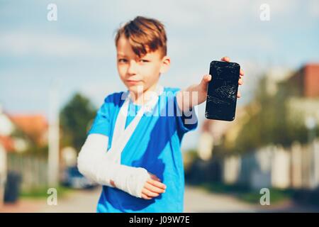 Petit garçon avec fracture de la main blessé après accident montrant téléphone mobile endommagé Banque D'Images