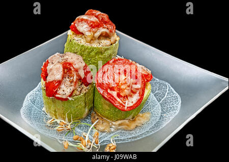 Les courgettes farcies aux légumes et riz avec des tomates avec le germe de blé et parmesan plat végétarien sur le verre de la plaque carrée isolated on black Banque D'Images