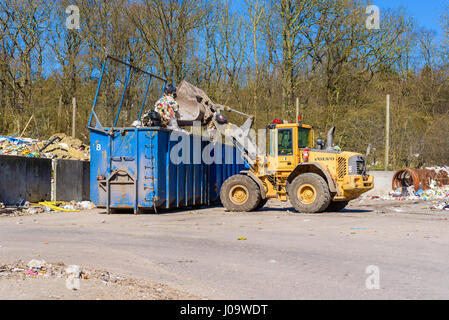 Ronneby, Suède - le 27 mars 2017 : Documentaire de gaspillage de fonds publics. Volvo L90e corbeille Vidage de chargeur sur roues en bleu contenant. Banque D'Images