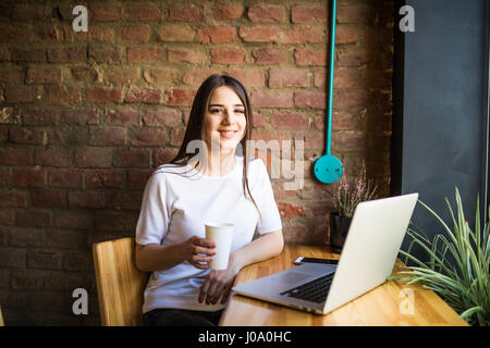 Portrait d'une jeune belle businesswomen bénéficiant du café pendant le travail sur ordinateur portable, charmante étudiante à l'aide de net-book pendant que le STIT Banque D'Images