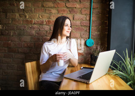 Portrait d'une jeune belle businesswomen bénéficiant du café pendant le travail sur ordinateur portable, charmante étudiante à l'aide de net-book pendant que le STIT Banque D'Images