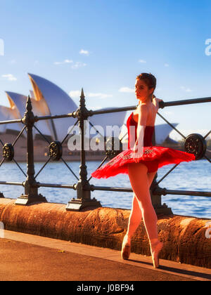 Street dance performing ballerine en rouge les concerts danse tutu au point de chaussures à une clôture du port de Sydney en rayons chauds du soleil du matin. Banque D'Images
