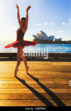 Mettre en place les jeunes en concert tutu ballerine rouge danse sur un trottoir de bois dans Sydney The Rocks lieu au bord de l'eau du port de Sydney par temps chaud soleil levant r Banque D'Images