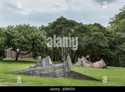 Auckland, Nouvelle-Zélande - 1 mars, 2017 : collection de statues dans le parc de l'Ouest font semblant d'être des morceaux de façades en pierre à moitié enfoui dans la pelouse verte. Tree Banque D'Images