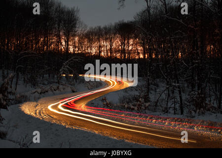 S courbe sur une route forestière, la nuit, l'hiver, juste après le coucher du soleil. Les lumières sont créés par le passage des voitures. Banque D'Images