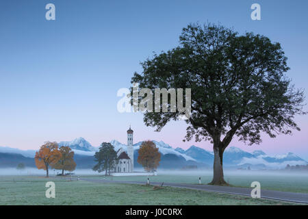 Lever et Rose brume d'automne sur l'église Saint Coloman encadrée par des sommets enneigés, Schwangau, Bavière, Allemagne Banque D'Images