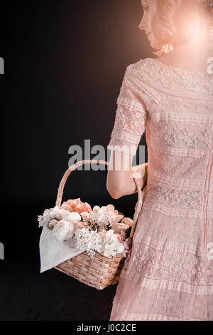 Vue arrière de jeune femme en robe rose marcher avec panier de fleurs Banque D'Images