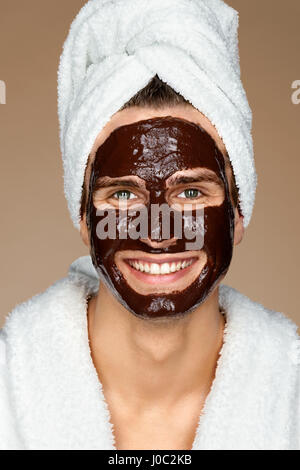 Homme heureux avec masque au chocolat sur son visage. Photo de laughing man recevant des soins spa. Le toilettage lui-même Banque D'Images