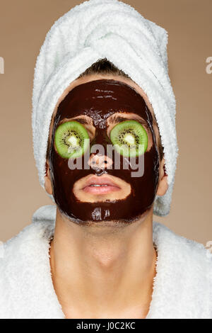 L'homme chocolat avec Mack et tranches de kiwi sur les yeux. Portrait de bel homme recevant des soins spa. Concept de soins de la peau Banque D'Images