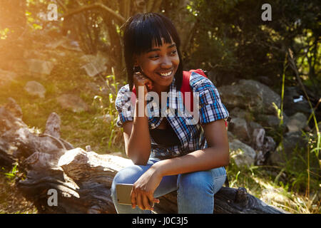 Jeune femme dans la forêt, assis sur l'arbre tombé, holding smartphone, Cape Town, Afrique du Sud Banque D'Images