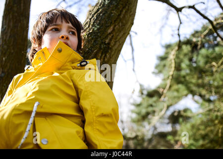 Garçon en anorak jaune appuyé contre park tree Banque D'Images