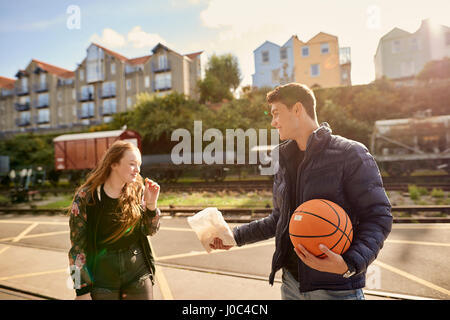 Jeune homme partager sac de croustilles avec ami, young man holding basket-ball, Bristol, UK Banque D'Images